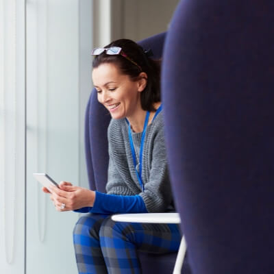 /sitecore/media library/Australia/Images/covered-images/Home/Woman typing into mobile phone sitting forward on big chair smiling